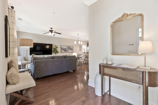 living room with ceiling fan with notable chandelier, dark wood-type flooring, and baseboards