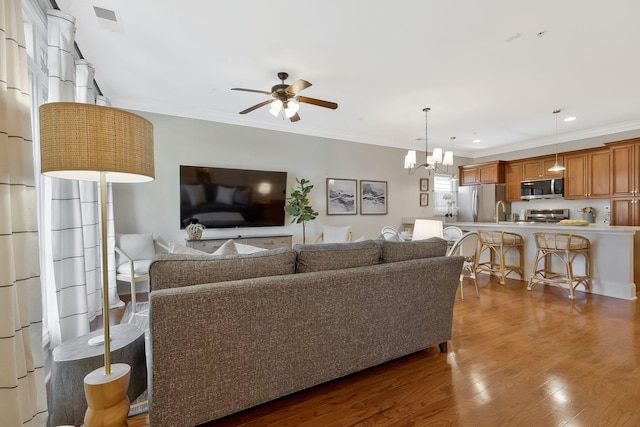 living area with crown molding, recessed lighting, visible vents, wood finished floors, and ceiling fan with notable chandelier