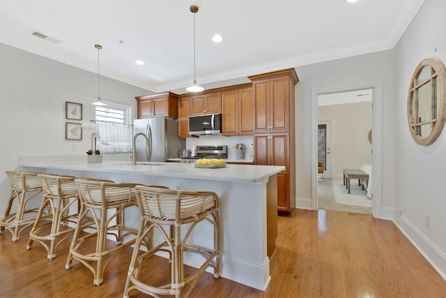 kitchen featuring light wood-style flooring, appliances with stainless steel finishes, brown cabinets, light countertops, and a kitchen bar