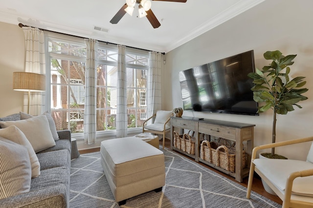 living area with a ceiling fan, wood finished floors, visible vents, and crown molding