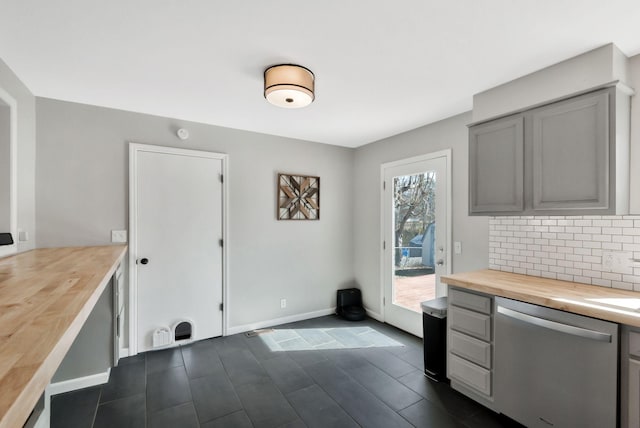 kitchen with baseboards, decorative backsplash, butcher block counters, gray cabinetry, and stainless steel dishwasher