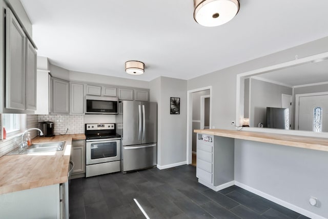 kitchen with butcher block counters, a sink, baseboards, appliances with stainless steel finishes, and decorative backsplash