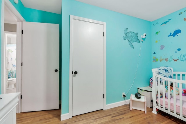 bedroom featuring a crib, light wood-style floors, and baseboards