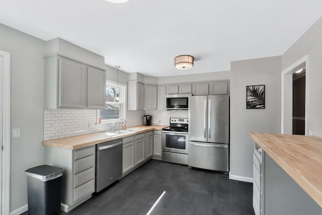 kitchen with baseboards, wood counters, appliances with stainless steel finishes, a sink, and backsplash