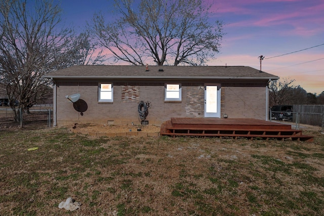 back of property at dusk featuring brick siding, a lawn, crawl space, fence, and a deck