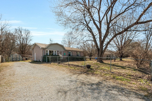 view of front of house with a storage shed, driveway, a fenced front yard, and an outbuilding