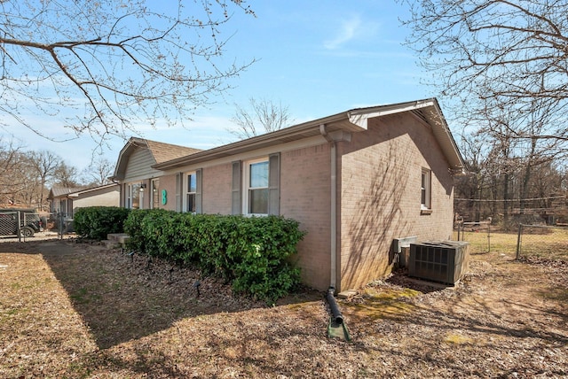 view of side of property featuring brick siding, fence, and central AC unit