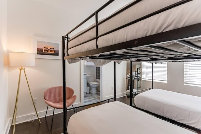 bedroom with ensuite bathroom, wood finished floors, and baseboards