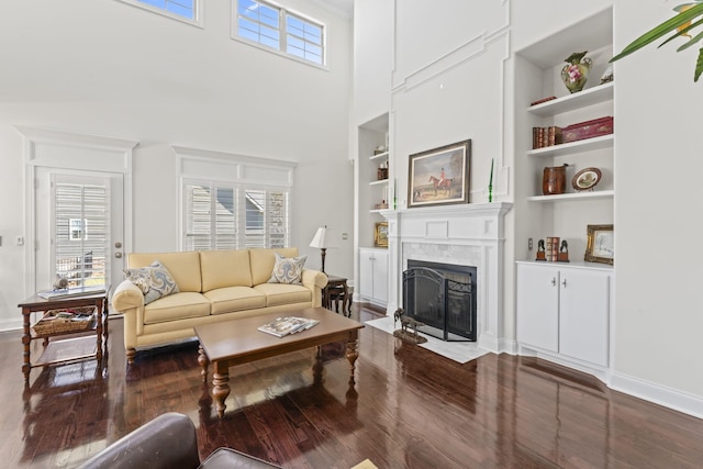 living area featuring baseboards, built in features, a towering ceiling, a fireplace with flush hearth, and wood finished floors