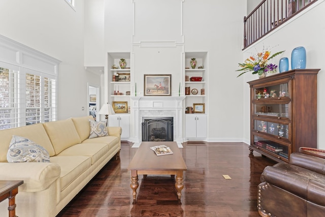 living area featuring built in features, a fireplace, a towering ceiling, wood finished floors, and baseboards