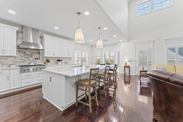 kitchen with tasteful backsplash, dark wood-style flooring, wall chimney range hood, stainless steel gas cooktop, and a sink