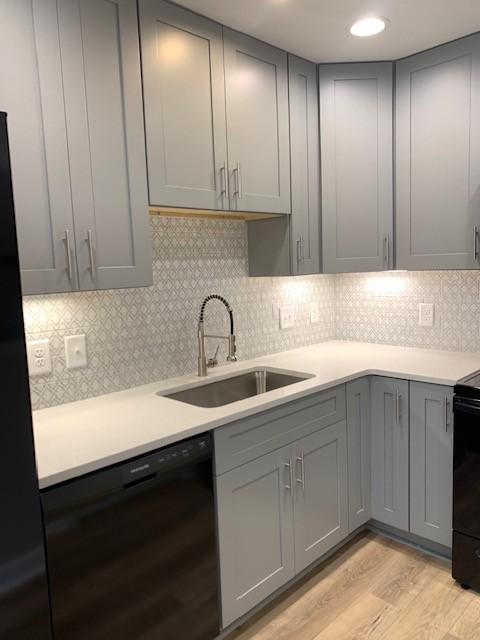 kitchen featuring gray cabinets, light countertops, light wood-style floors, a sink, and black appliances