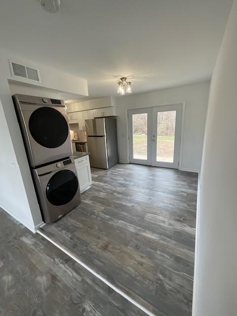 laundry area with french doors, dark wood-style flooring, stacked washer and dryer, visible vents, and baseboards