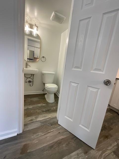 half bathroom with baseboards, toilet, and wood finished floors