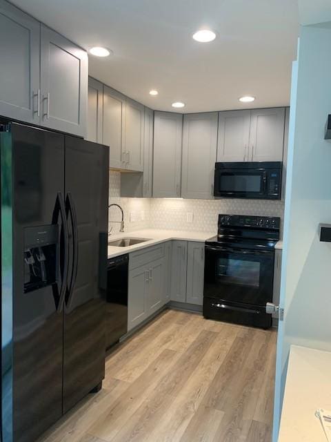 kitchen with a sink, gray cabinets, black appliances, light wood finished floors, and tasteful backsplash