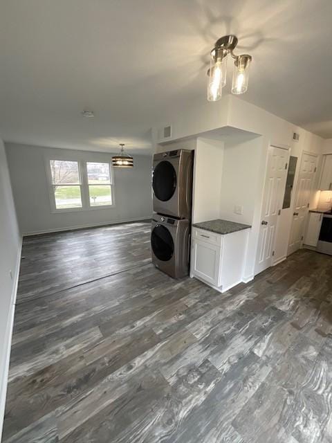 washroom featuring dark wood-type flooring, stacked washer / drying machine, laundry area, and baseboards