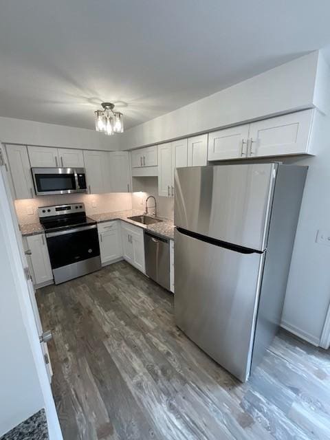 kitchen with stainless steel appliances, an inviting chandelier, white cabinetry, a sink, and wood finished floors