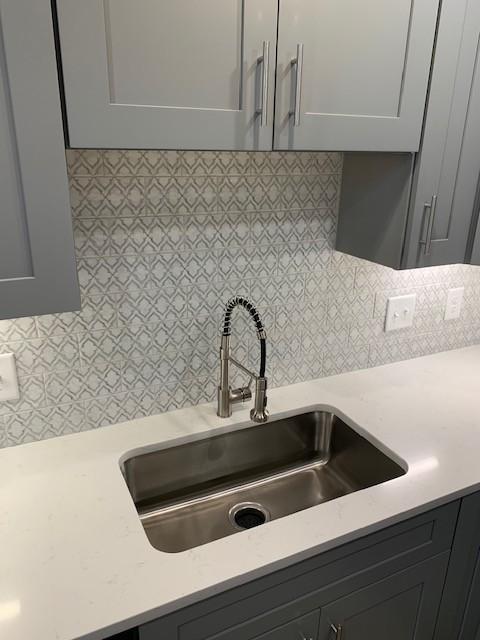 kitchen with gray cabinetry, light countertops, a sink, and decorative backsplash