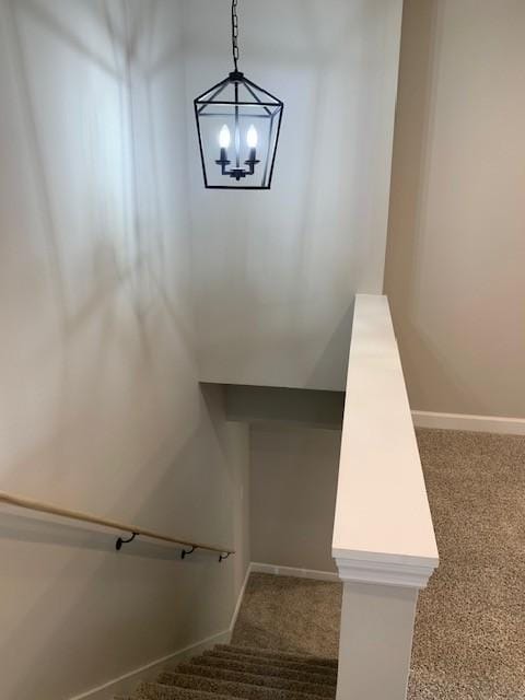 stairway featuring baseboards, a chandelier, and carpet flooring