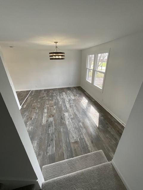 unfurnished dining area featuring an inviting chandelier, wood finished floors, and baseboards