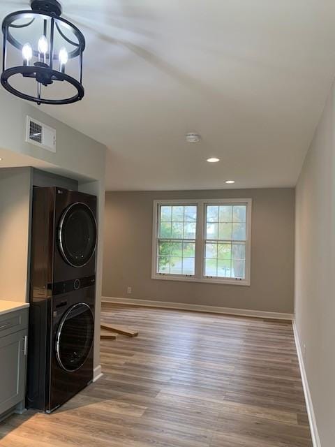 clothes washing area featuring a chandelier, light wood-style flooring, stacked washer / dryer, visible vents, and baseboards