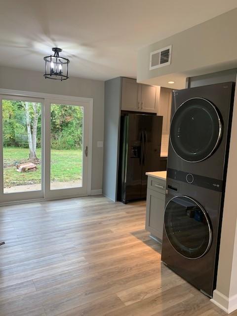 laundry room with a chandelier, laundry area, visible vents, light wood-style floors, and stacked washer / drying machine