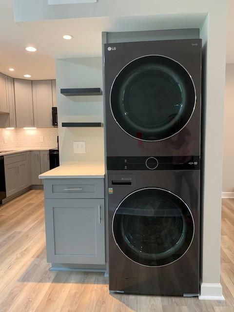 laundry area with recessed lighting, laundry area, light wood-style flooring, and stacked washing maching and dryer