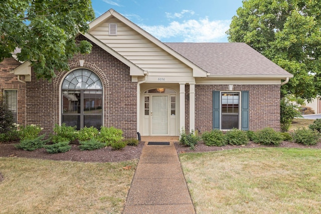 view of front of house featuring brick siding, roof with shingles, and a front yard