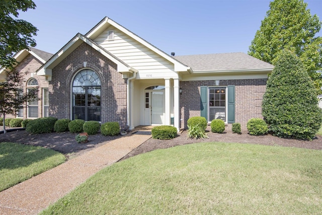 view of front of home with brick siding, roof with shingles, and a front yard