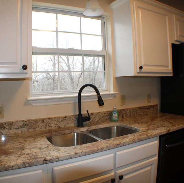 kitchen featuring freestanding refrigerator, light stone counters, a sink, and white cabinetry