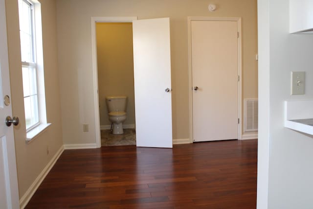 unfurnished bedroom featuring baseboards, visible vents, multiple windows, and wood finished floors