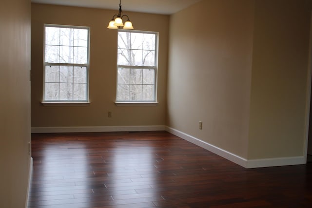 spare room featuring dark wood-type flooring, a notable chandelier, and baseboards