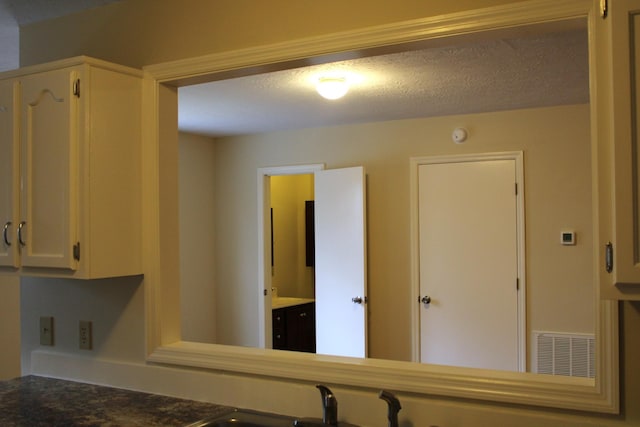 interior space with visible vents, a textured ceiling, and white cabinetry