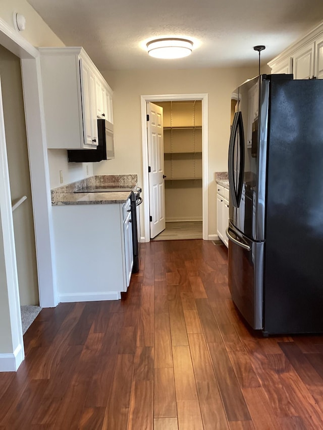 kitchen featuring baseboards, dark wood-type flooring, freestanding refrigerator, stone counters, and white cabinetry