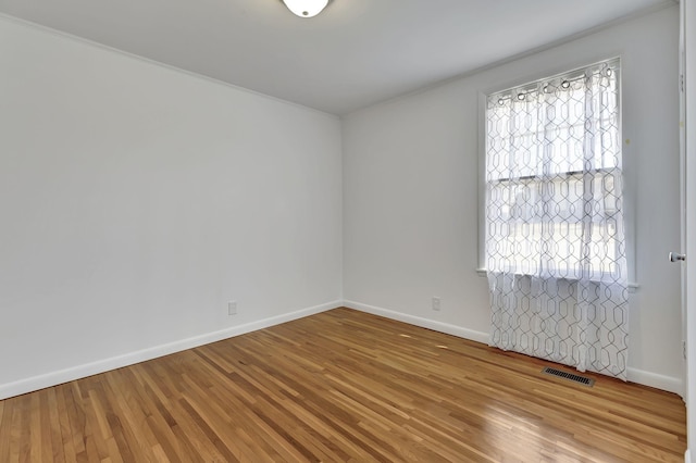 unfurnished room featuring a healthy amount of sunlight, visible vents, baseboards, and wood finished floors