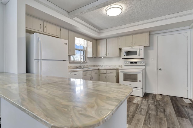 kitchen with a textured ceiling, a peninsula, white appliances, a sink, and dark wood finished floors