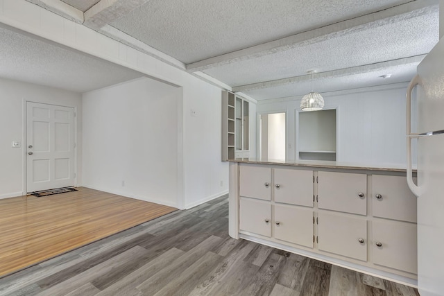 spare room featuring a textured ceiling, wood finished floors, beam ceiling, and baseboards