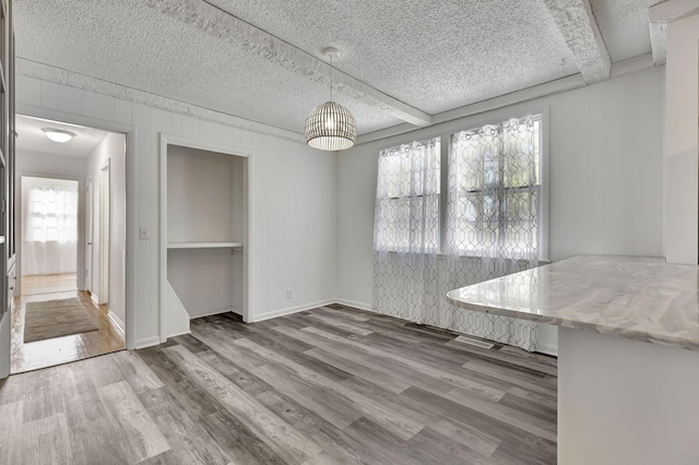 unfurnished dining area with a textured ceiling, wood finished floors, and beam ceiling