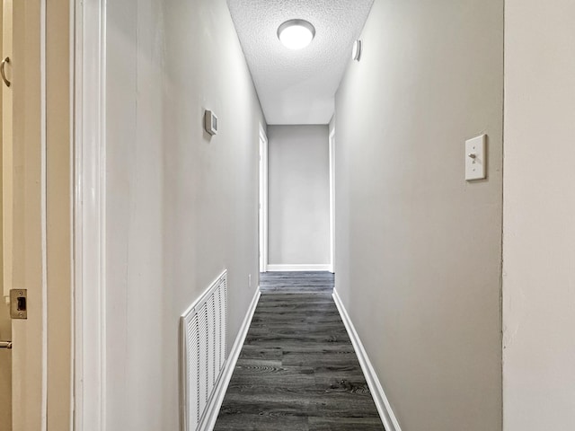 hallway with a textured ceiling, dark wood-style flooring, visible vents, and baseboards