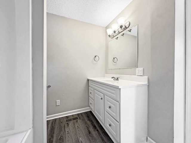 bathroom with a textured ceiling, wood finished floors, visible vents, vanity, and baseboards