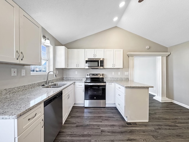 kitchen featuring dark wood finished floors, stainless steel appliances, white cabinets, a sink, and a peninsula