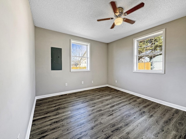 spare room featuring baseboards, dark wood-type flooring, electric panel, and a healthy amount of sunlight