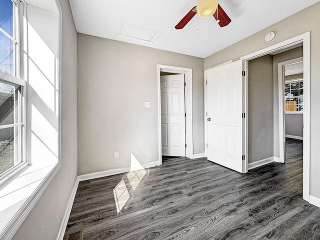 unfurnished bedroom featuring attic access, visible vents, baseboards, ceiling fan, and dark wood-type flooring