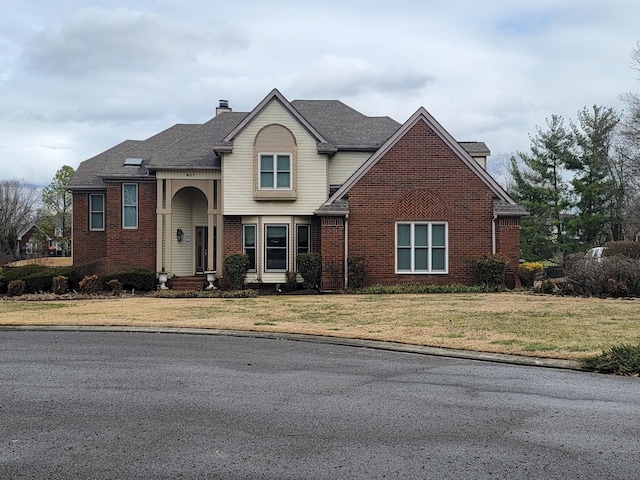 traditional-style house with a shingled roof, brick siding, a chimney, and a front lawn