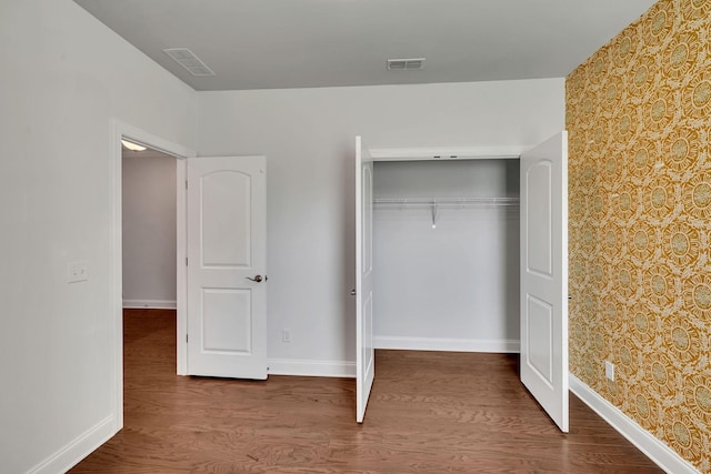 unfurnished bedroom featuring a closet, wood finished floors, visible vents, and baseboards