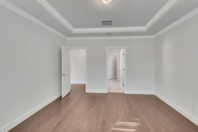 unfurnished bedroom with baseboards, visible vents, wood finished floors, a tray ceiling, and crown molding