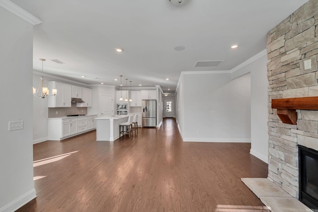 unfurnished living room featuring an inviting chandelier, dark wood-type flooring, ornamental molding, a stone fireplace, and baseboards