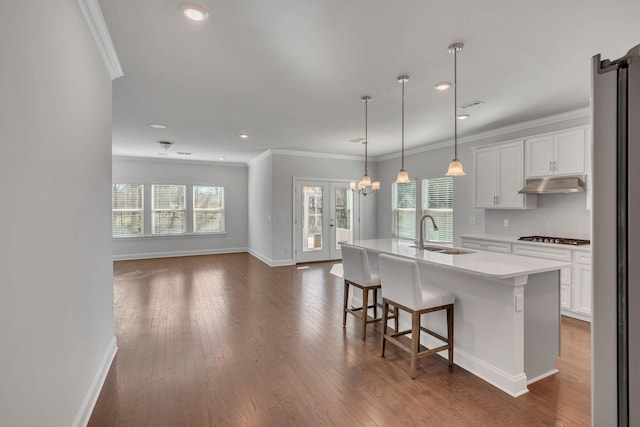 kitchen with light countertops, dark wood-type flooring, ornamental molding, a sink, and under cabinet range hood