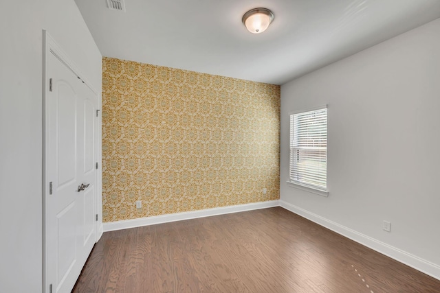 empty room featuring baseboards, dark wood finished floors, visible vents, and wallpapered walls