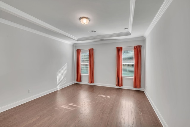 empty room with baseboards, visible vents, a tray ceiling, and wood finished floors